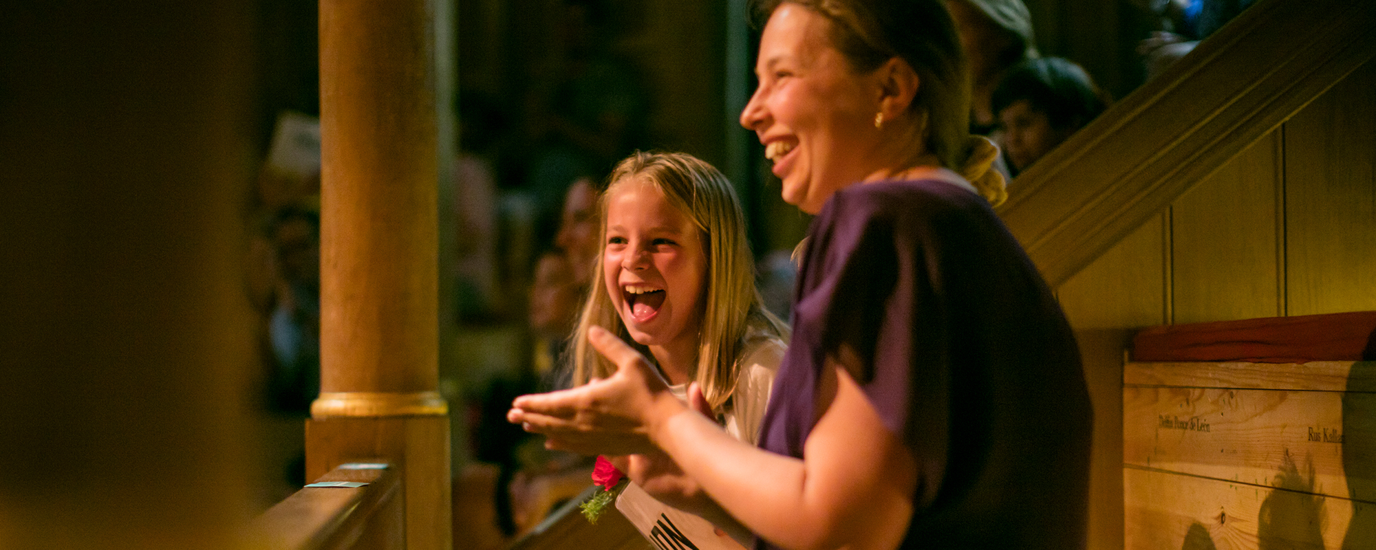 An adult and child clapping whilst watching a storytelling at the Sam Wanamaker Playhouse.
