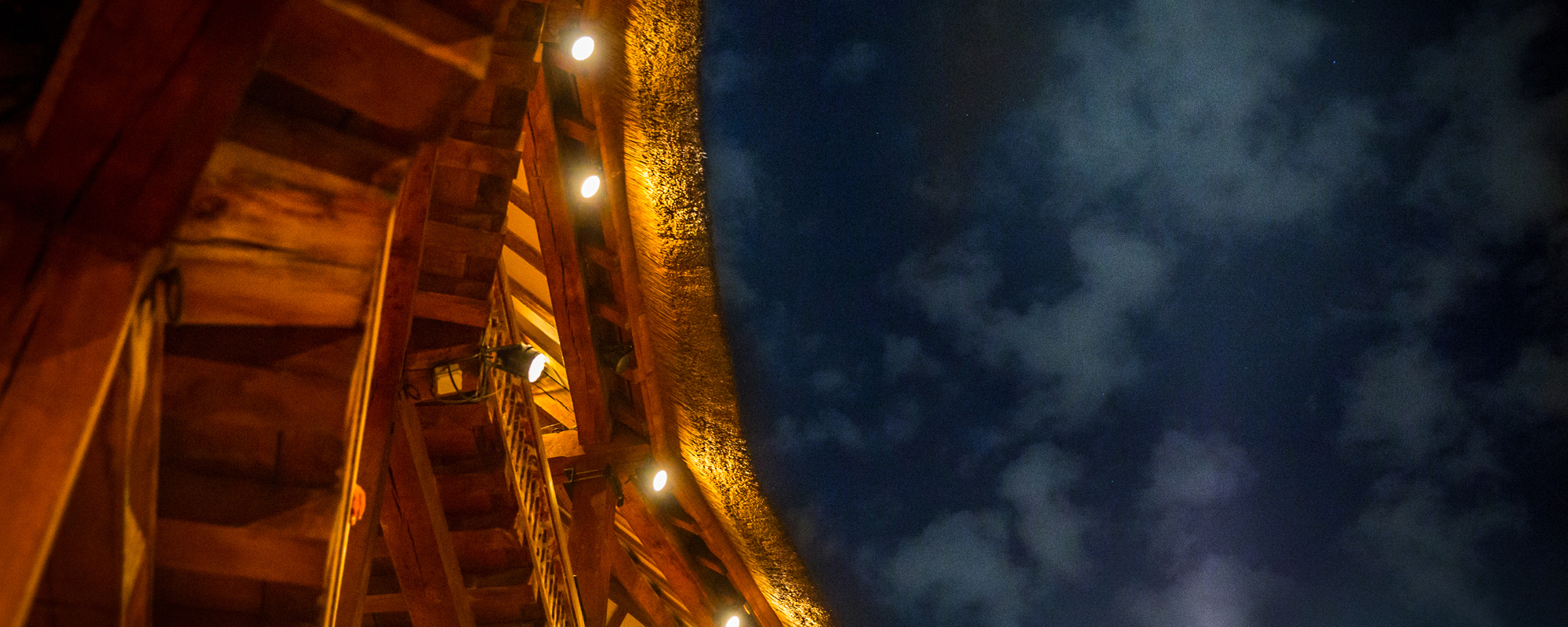 A close up of the corner of a roof of an open-air theatre, that shows an open sky and wooden beams