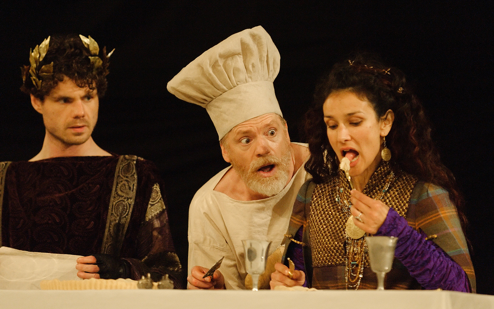 A man wearing a chef's hat watches as a woman raises a forkful of food to her mouth.