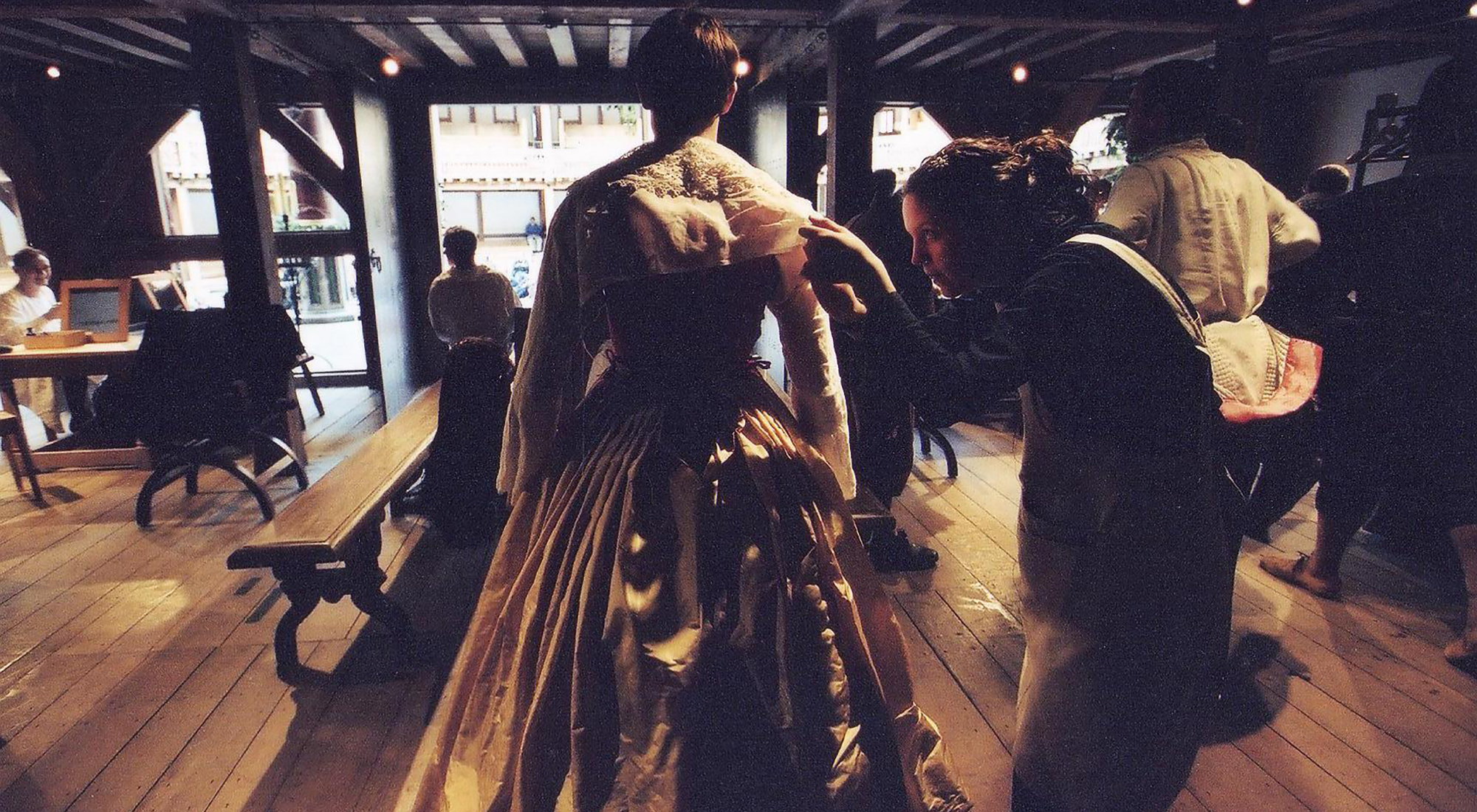 A backstage view of the Globe Theatre, wear a woman helps a man get in to his Elizabethan dress.