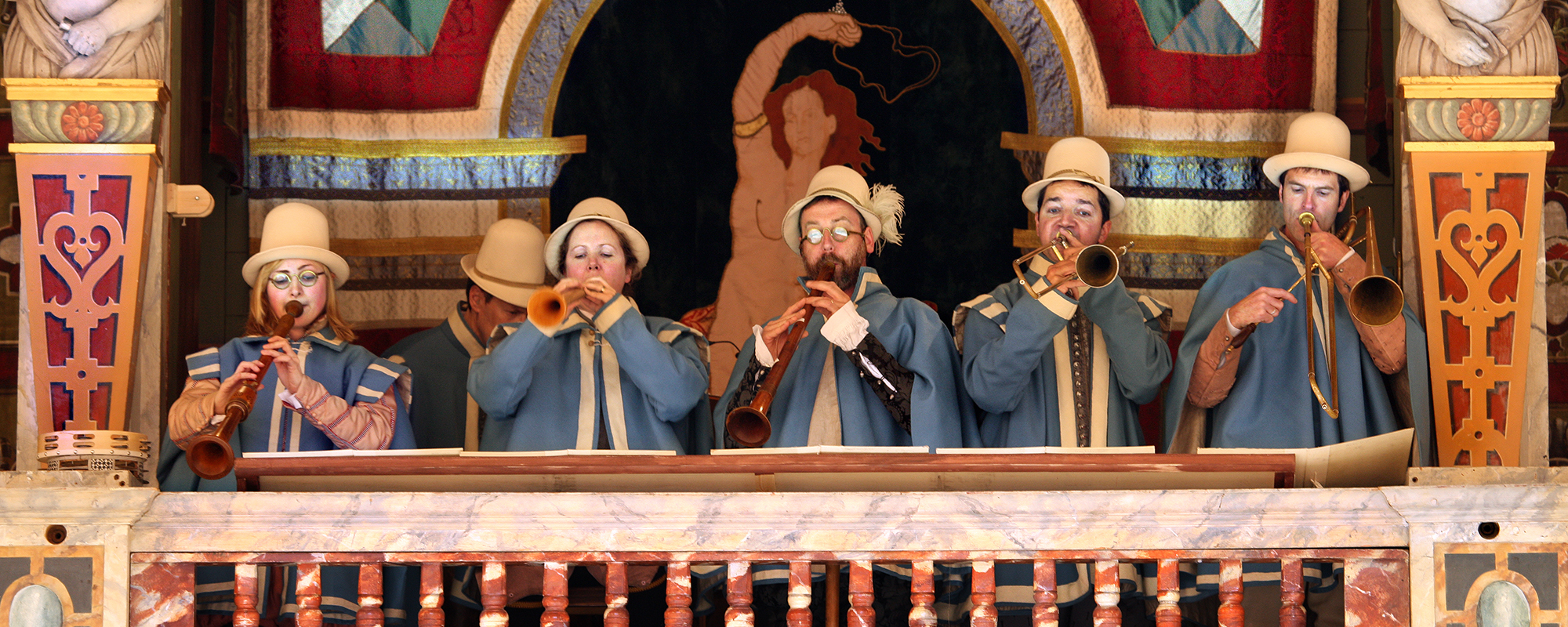 Five musicians stand in the gallery of the Globe Theatre, playing their musical instruments.