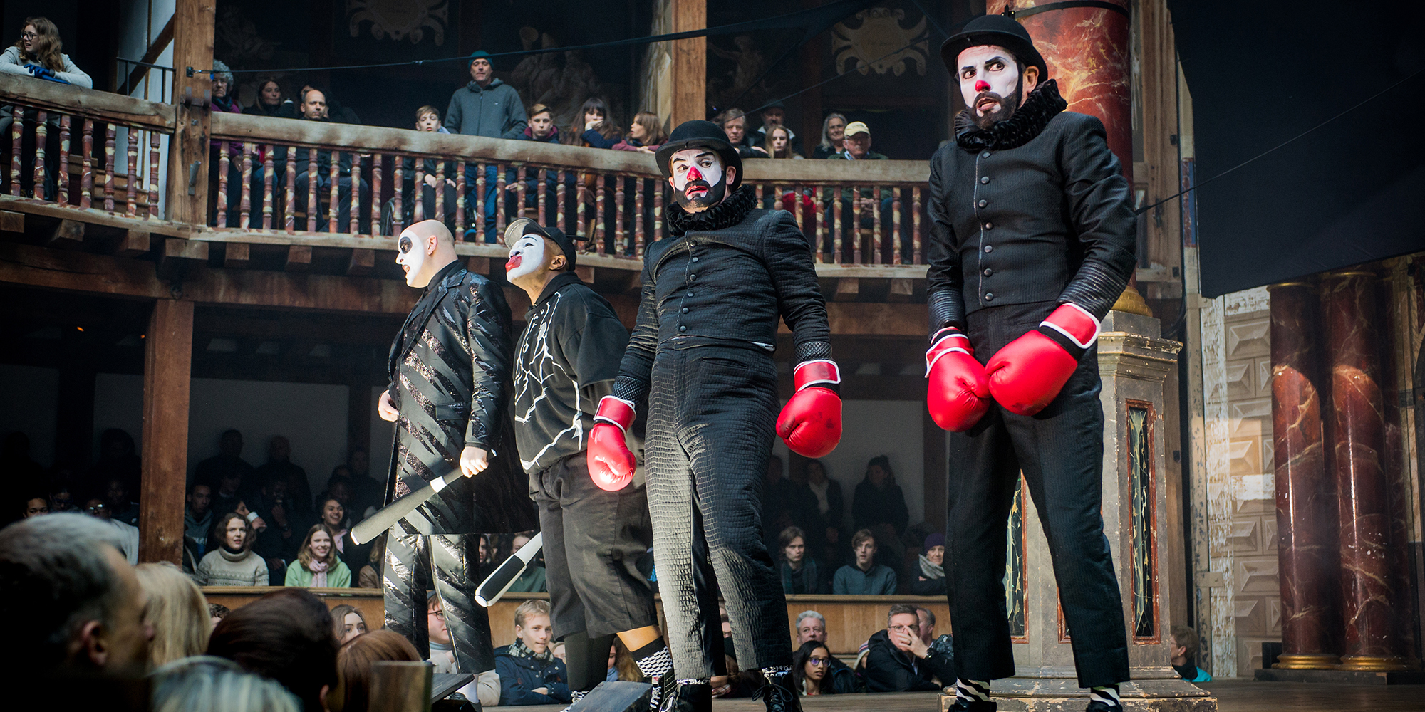 Four people wearing black, in clown makeup, and wearing red boxing gloves.