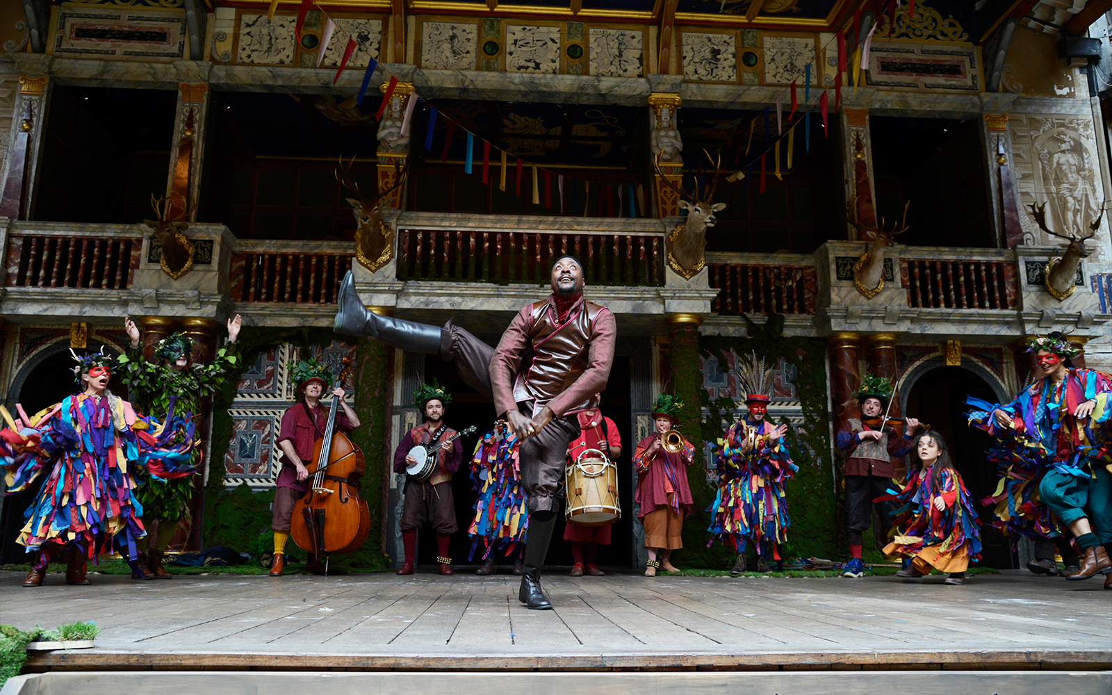 A actor kicks high in the air while others dance around him in colourful costumes