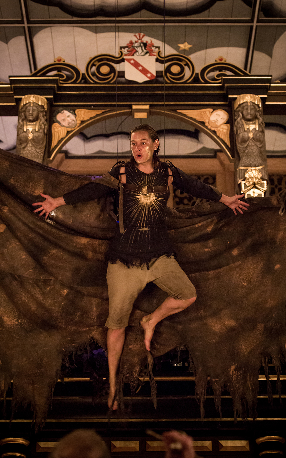A woman with large wings and a painted gold face, hangs in the air of the Sam Wanamaker Playhouse