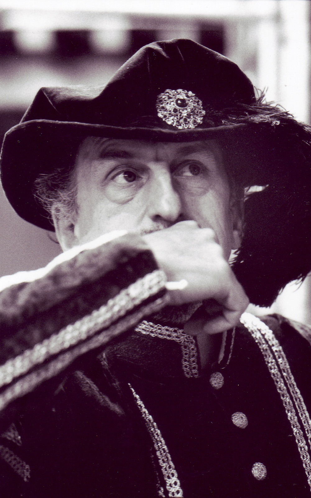 A man wearing a large hat leans his hand to his mouth.
