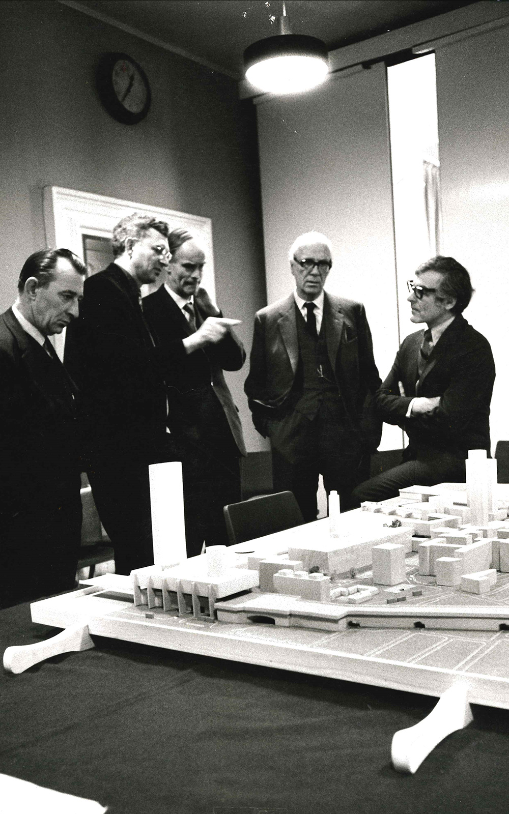 A group of men stand before a model plan of a development site