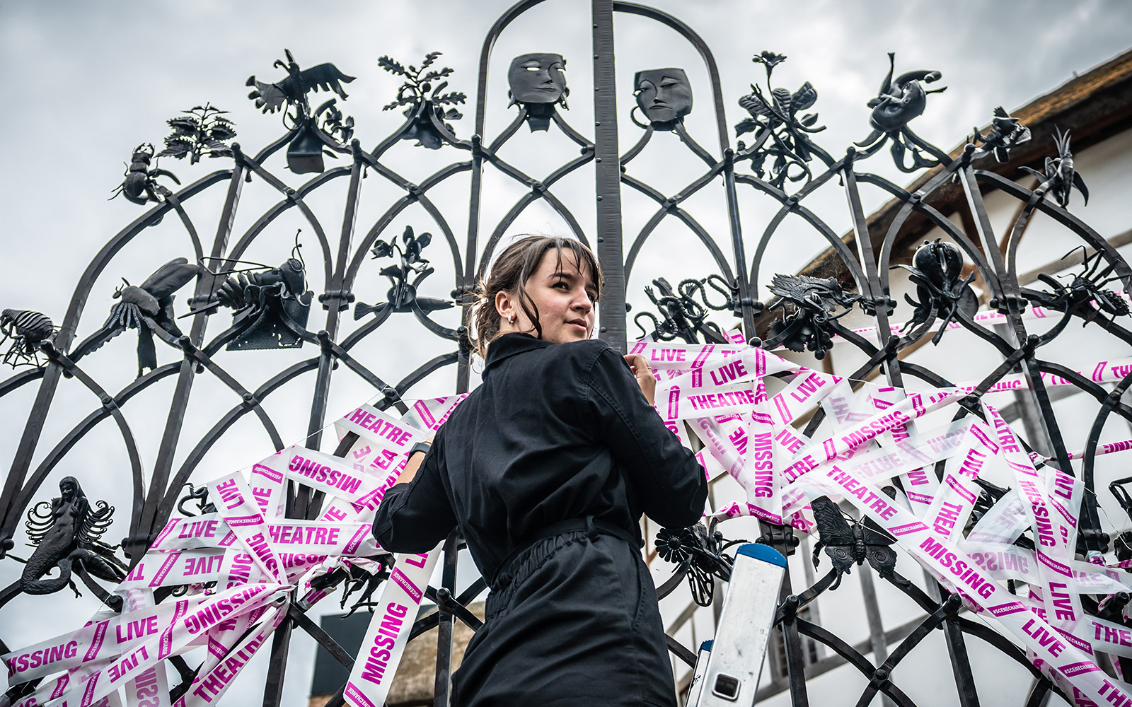 A shot looking up at a woman standing before a set of iron gates, placing white and pink tape.