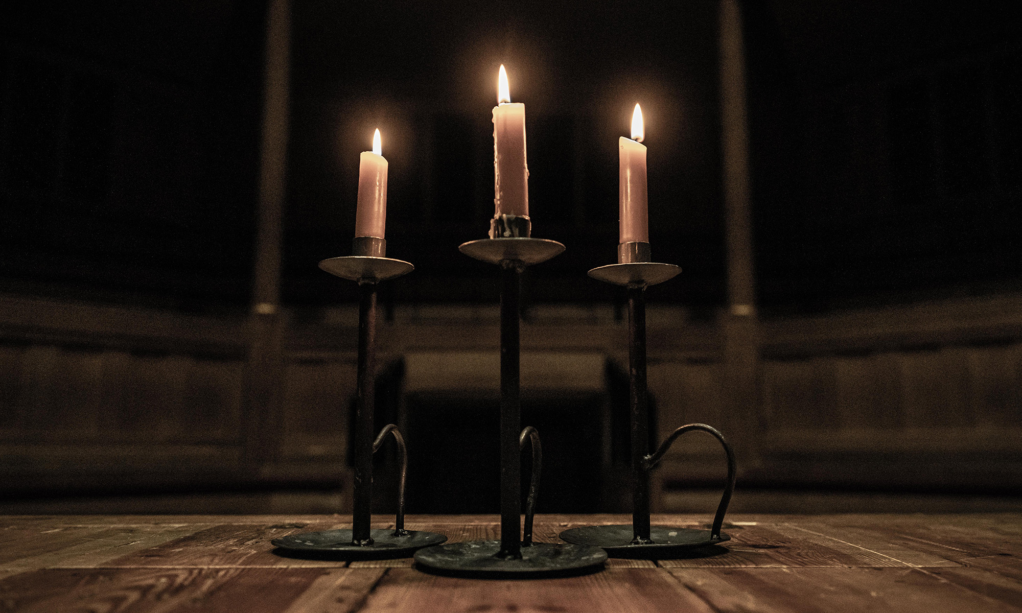 Three lit candles in the dark shadows of an indoor wooden theatre.