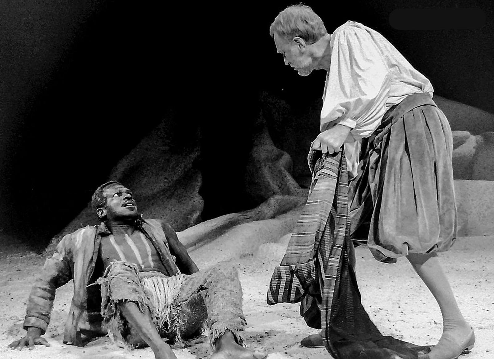 Rudolph Walker The Tempest The Old Vic Zuleika Henry 1988 A man sits on the floor, leaning back on his hands, staring fearfully at another man looming over him.