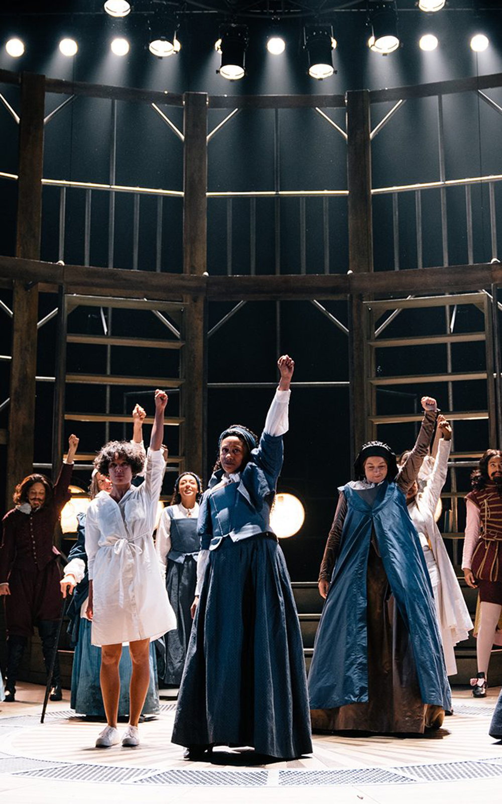 Globe Magazine Article Emilia 2019 Helen Murray A group of women hold their fists in the air on a dramatically lit stage
