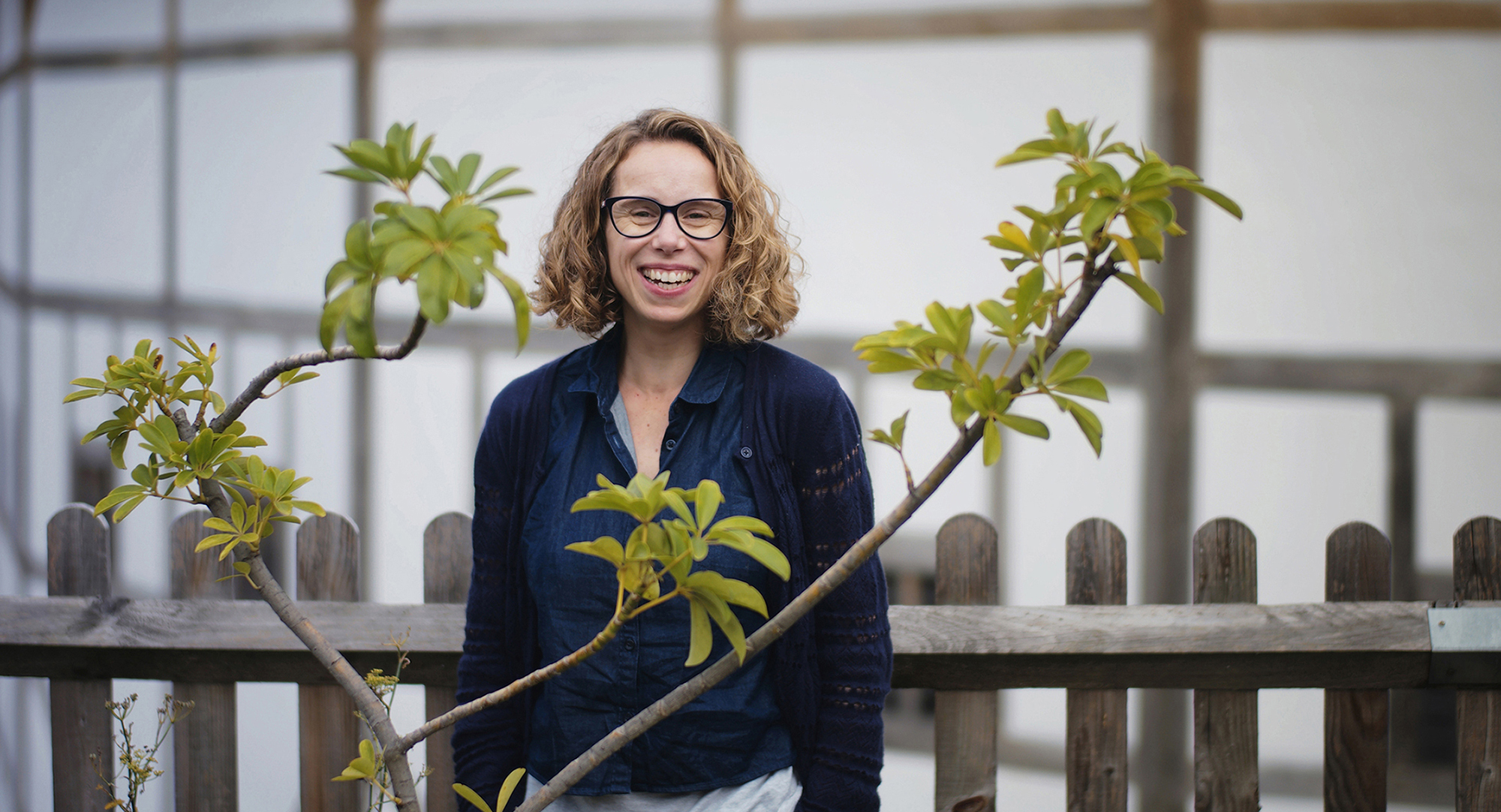 Globe Magazine Article Michelle Terry 2017 Photography Sarah Lee A woman smiles among trees foliage in front of a white building