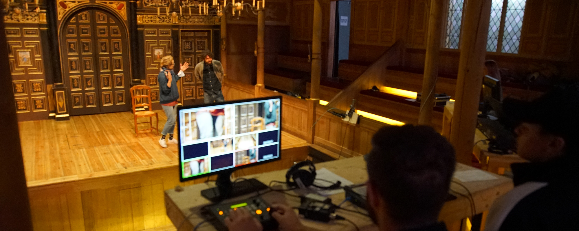 An image of the Sam Wanamaker PLayhouse with two actors rehearsing on the stage and a monitor showing different camera angles