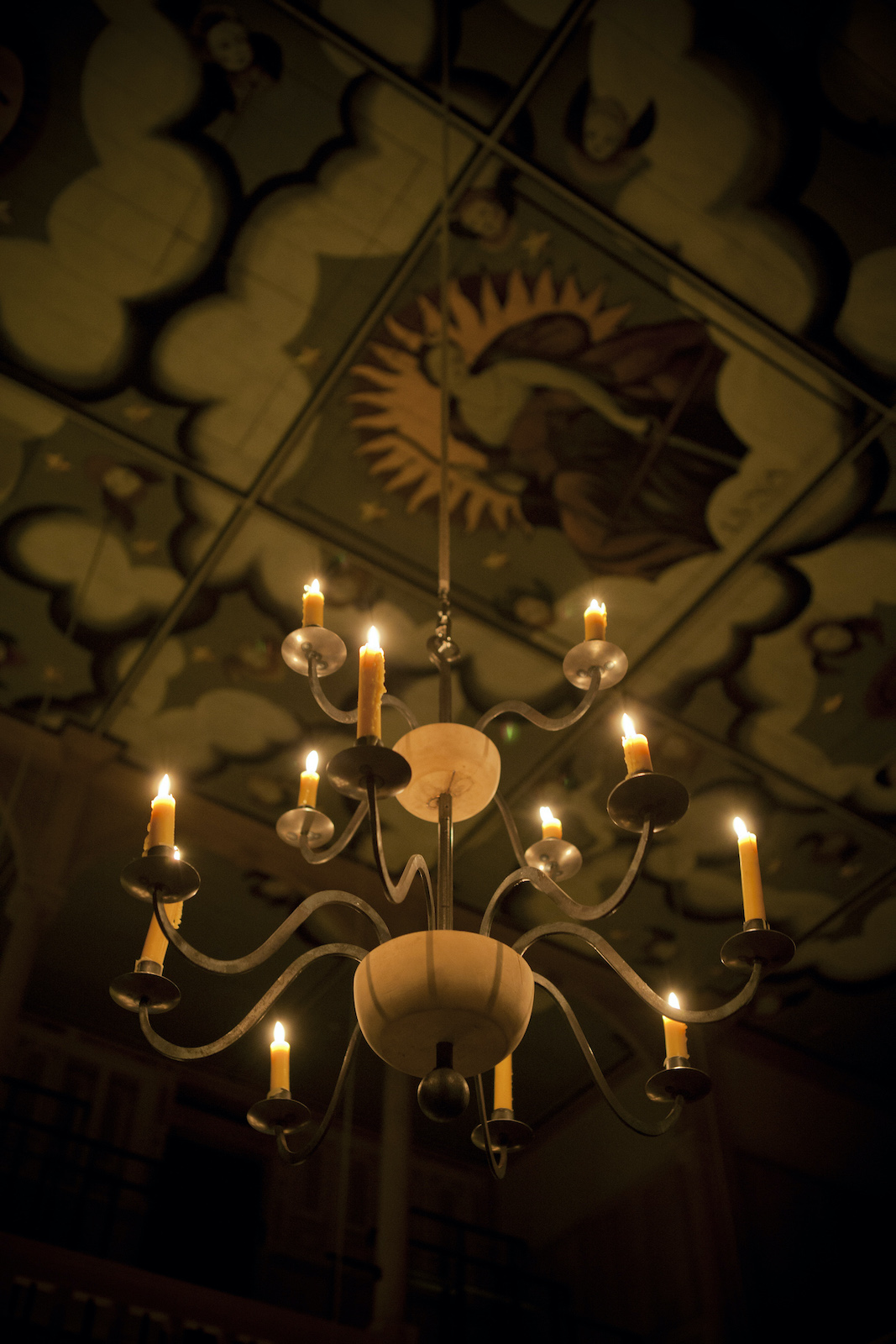 A lit candelabra hangs from a decorated ceiling.
