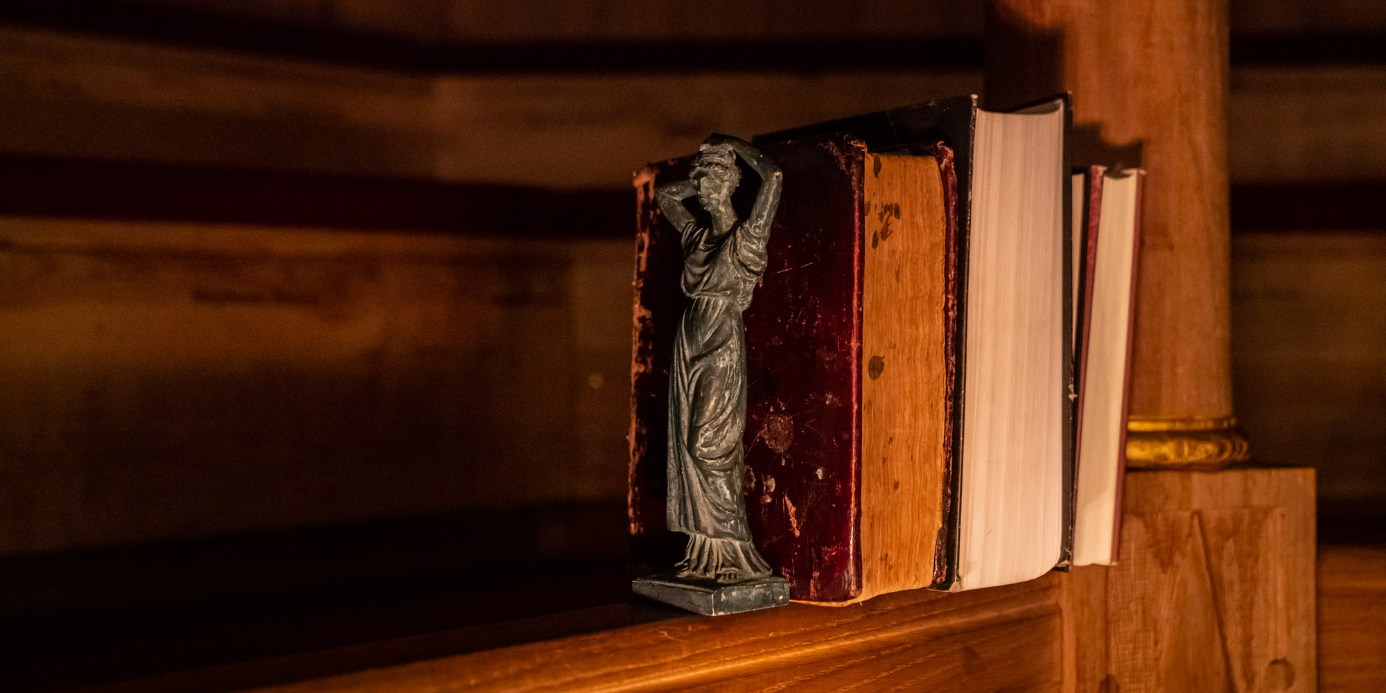 A row of books sits on the wooden gallery of the Sam Wanamaker Playhouse, cast in candlelight and shadows.