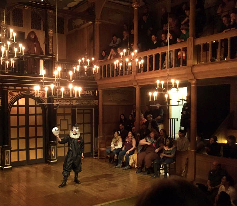 MollandtheFutureKings Anna Crisp 2 A drag artist wearing black doublet and hose, and holding a skull, stands in the candlelit Sam Wanamaker Playhouse.