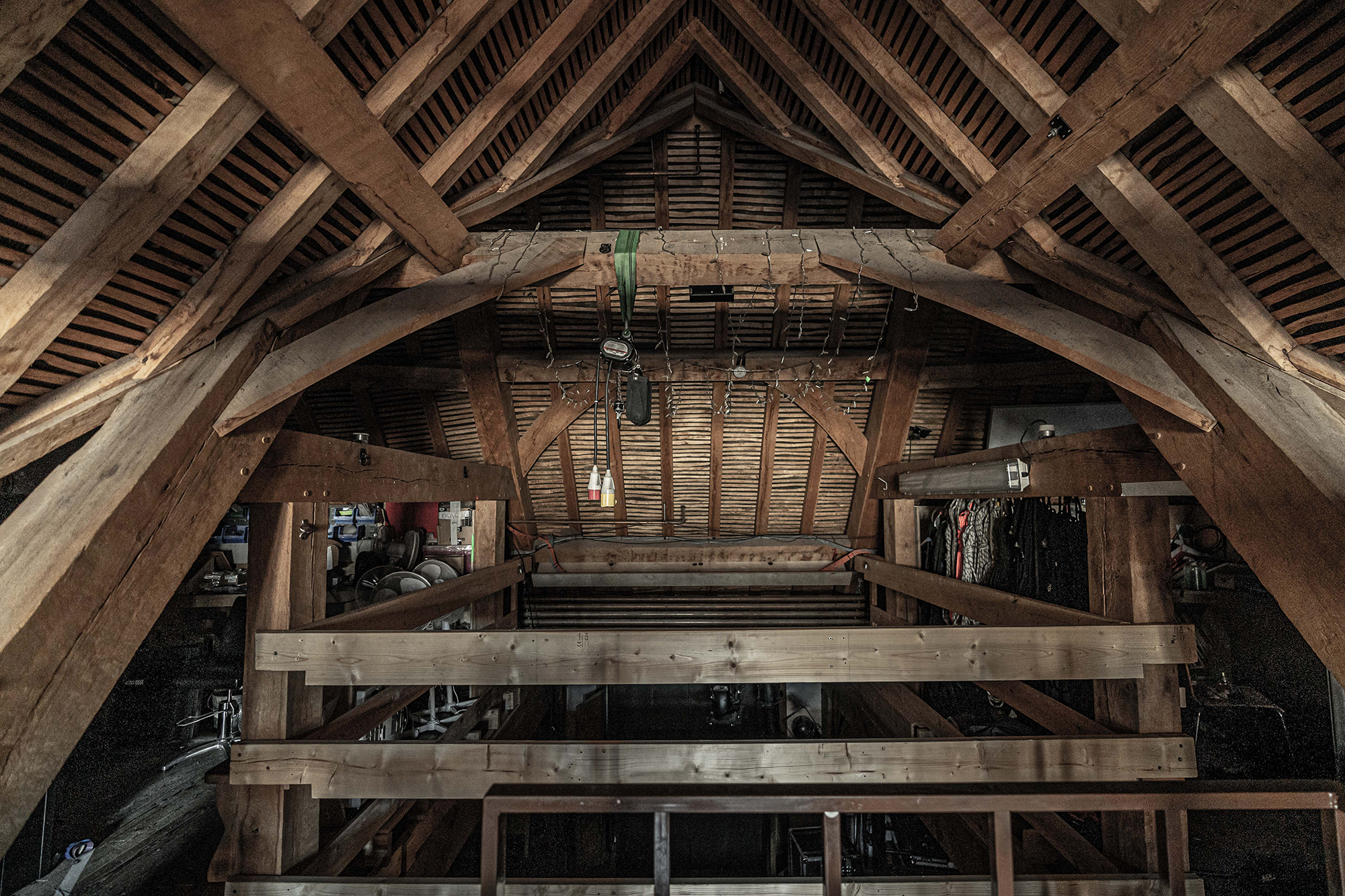 The inside of an attic with thatch roof and great oak beams. Various cables and objects hang from the rafters.