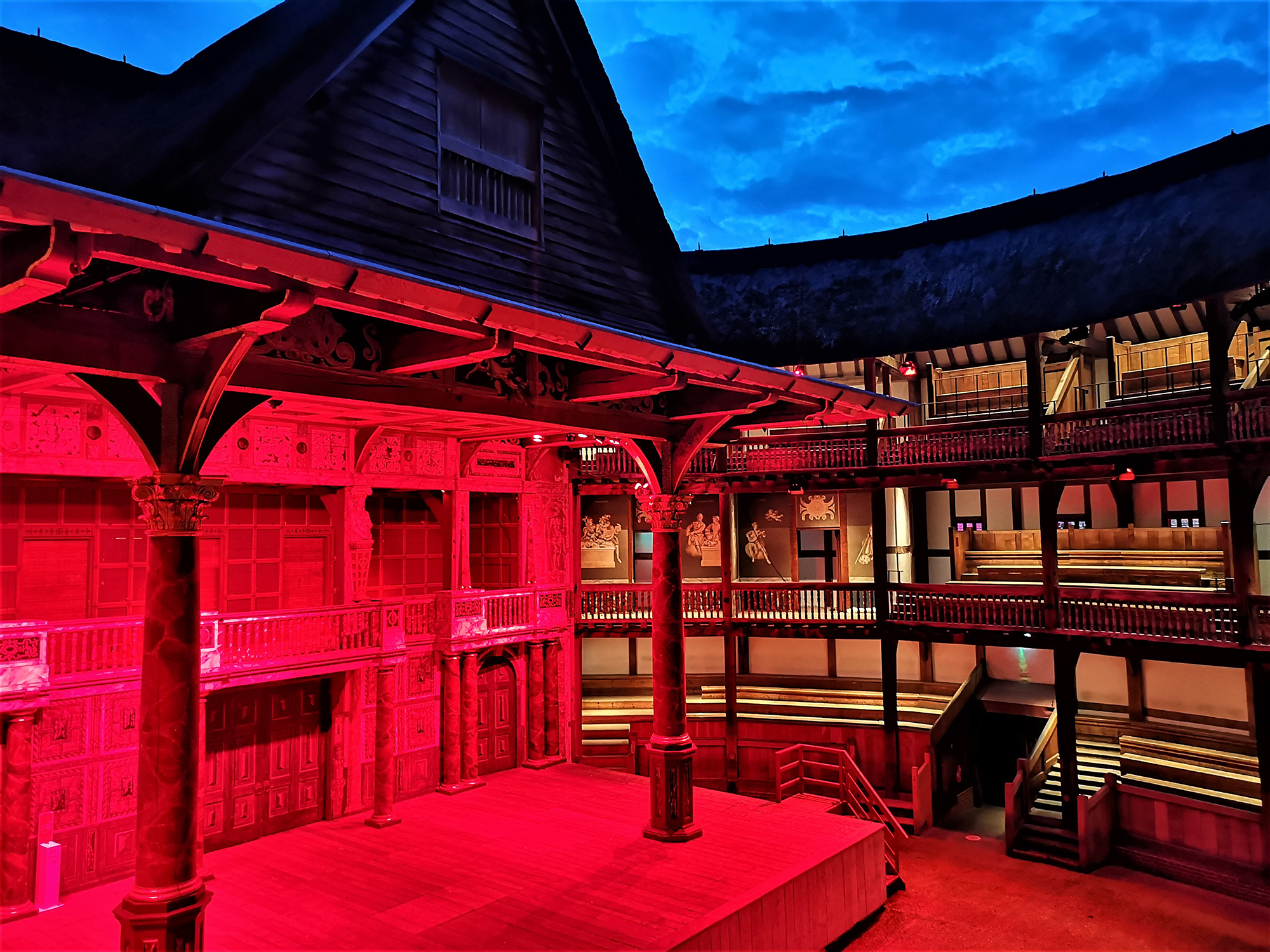 Light It In Red March 2021 Shakespeare's Globe 12 The stage of the Globe Theatre is lit by red lights.
