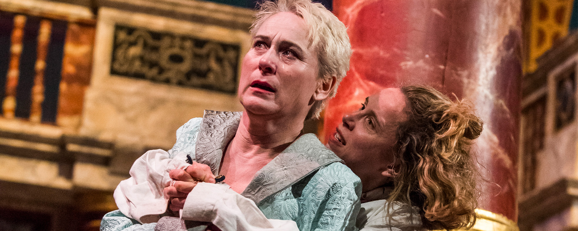 Mental Health Crisis 8 Episode 1 masthead An actor looks distressed on the globe stage while another actor wrap their arms round them in a sinister hug