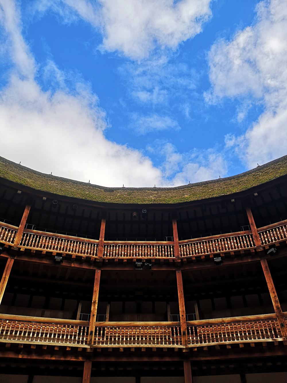 A bright blue sky, with streaks of clouds, above the timber tiered galleries of the Globe Theatre.