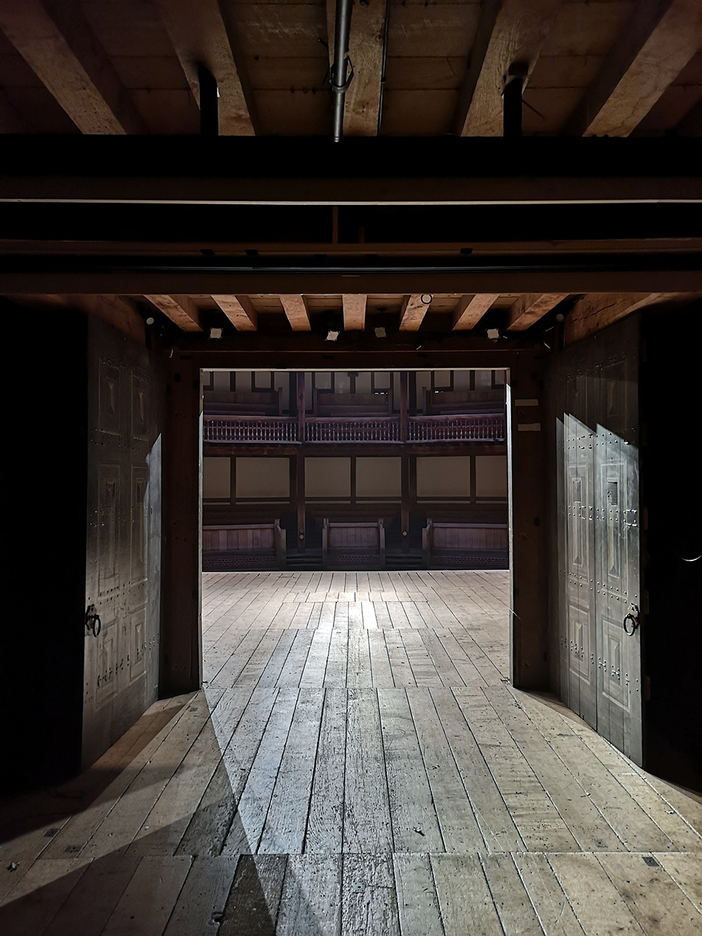 A view from backstage of the Globe Theatre, looking out through the open double oak doors on to the stage and the galleries beyond.