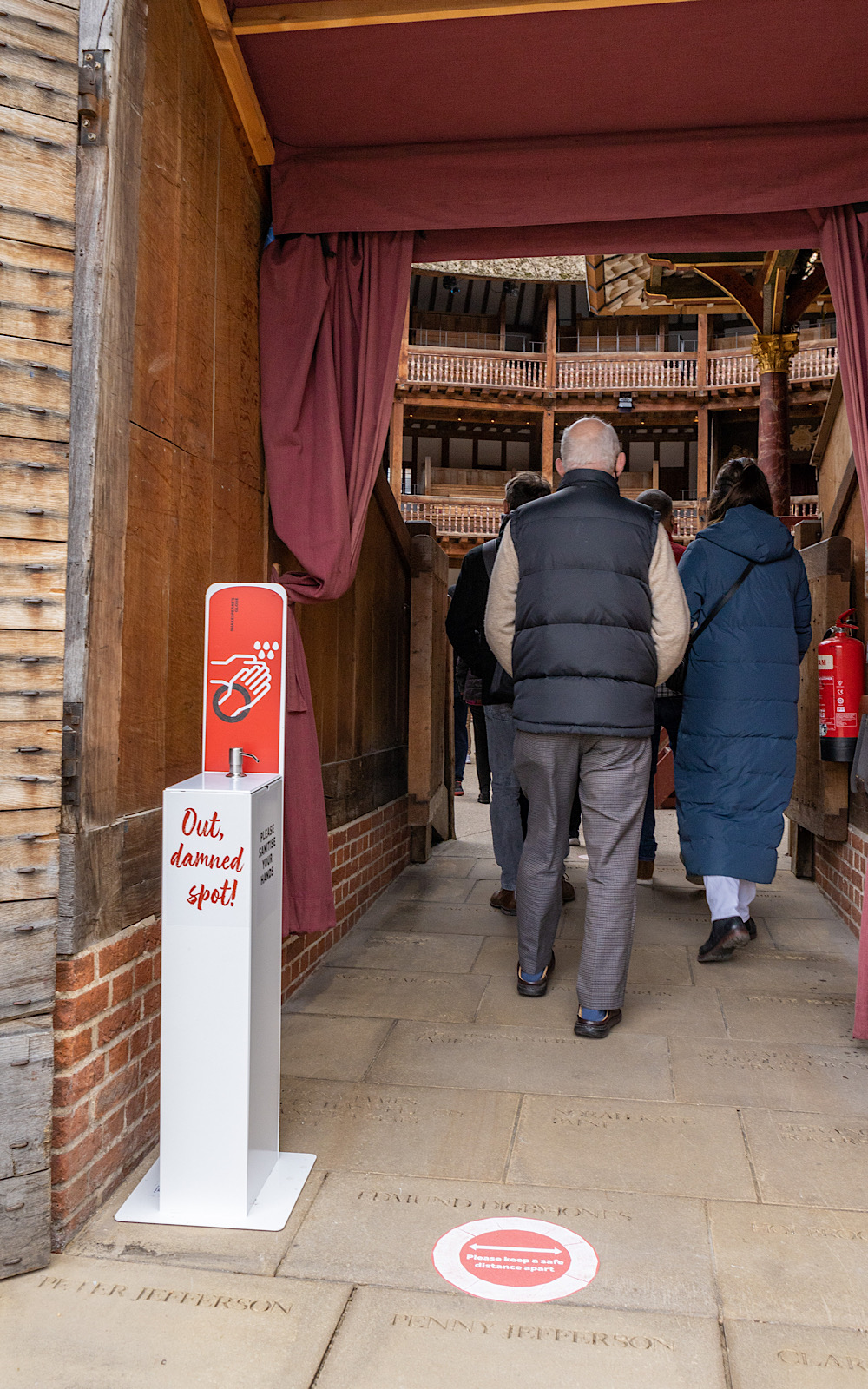 Guided Tours 2021 Pete Le May People walk through a door into an outdoor theatre and they walk past a hand sanitising station