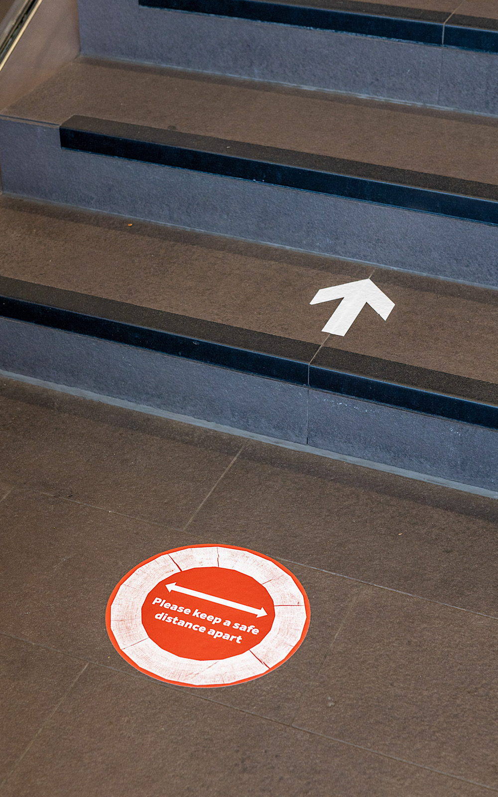 Covid Coronavirus Shakespeare’s Globe Pete Le May 2021 Stickers on a black floor show arrows and also notices to keep a safe distance from others