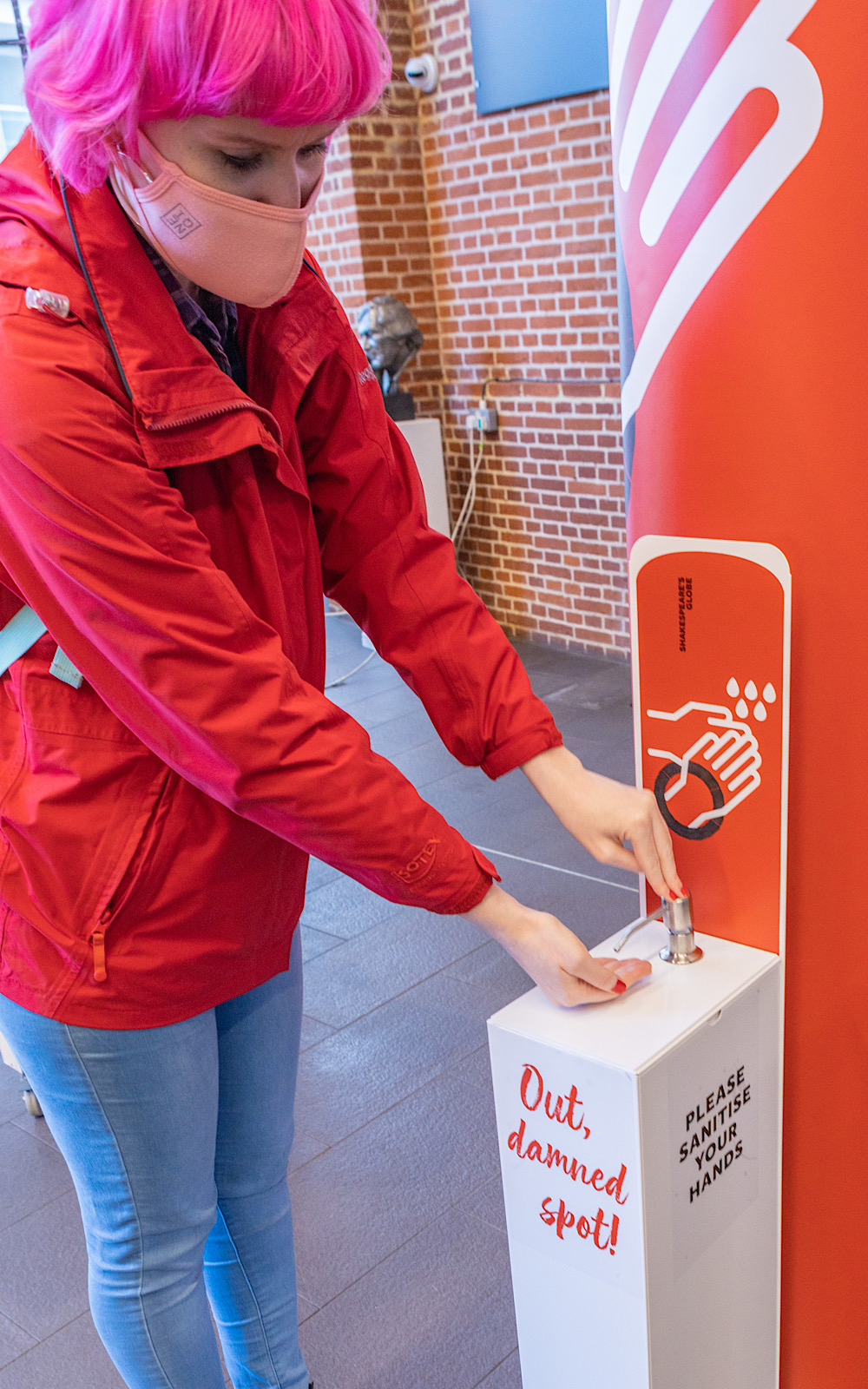 An audience member in a red jacket leans down to sanitise her hands at a sanitiser station