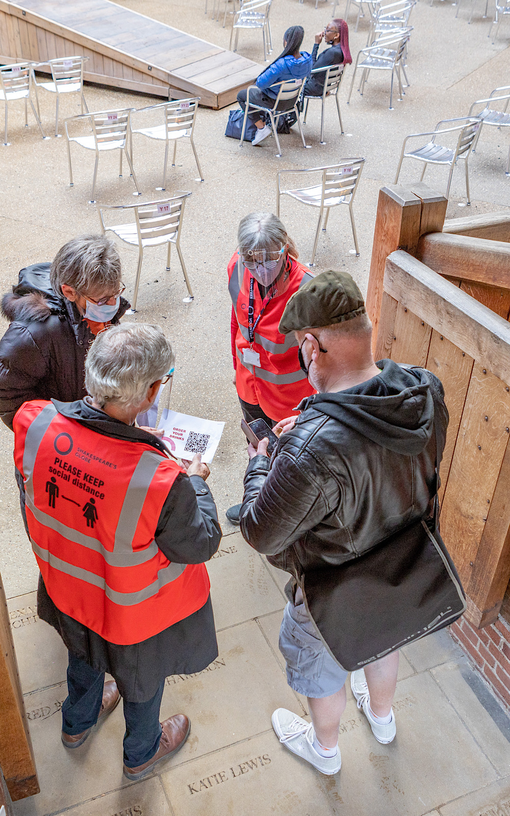 Members of staff in high-vis jackets talk to audience members as they enter an outdoor theatre