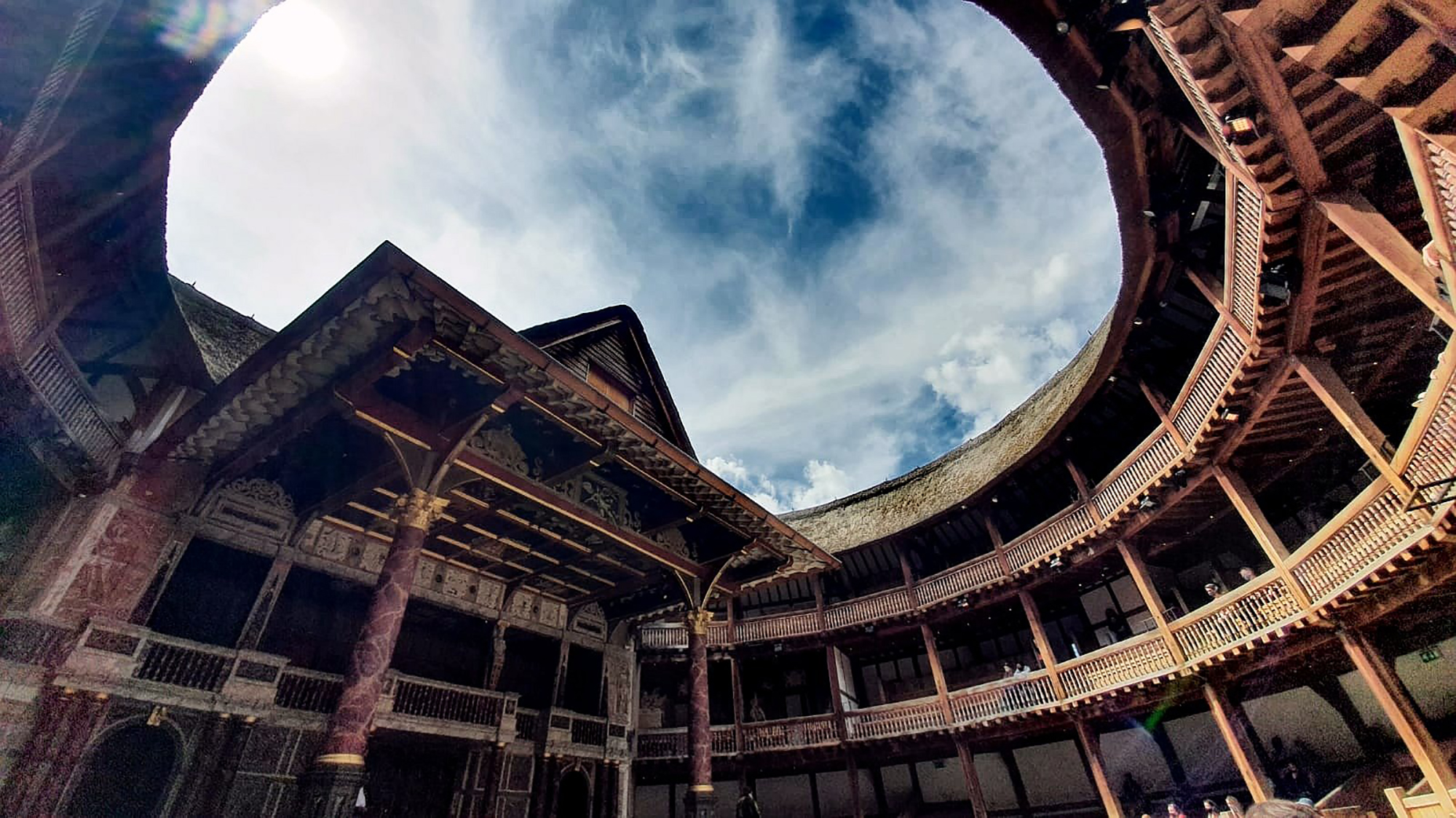 A blue sky streaked with wisps of white cloud above the circular timbre structure of the Globe Theatre.