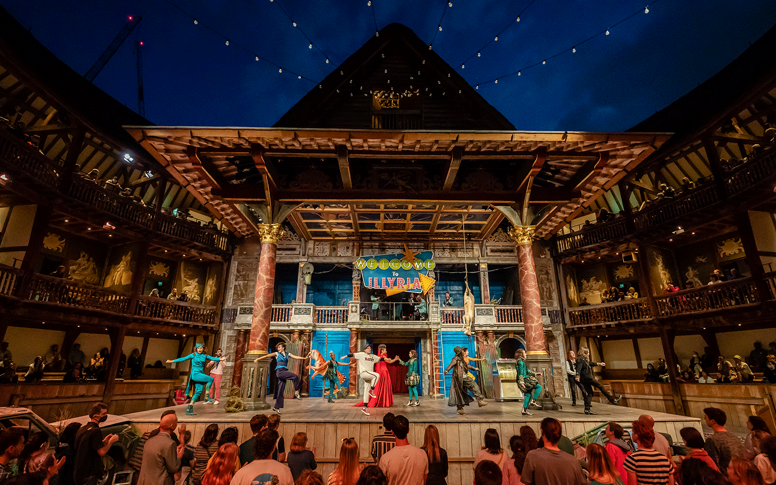 A dark cloudy night sky above the Globe Theatre stage: with fairy light hanging across the open-air roof.