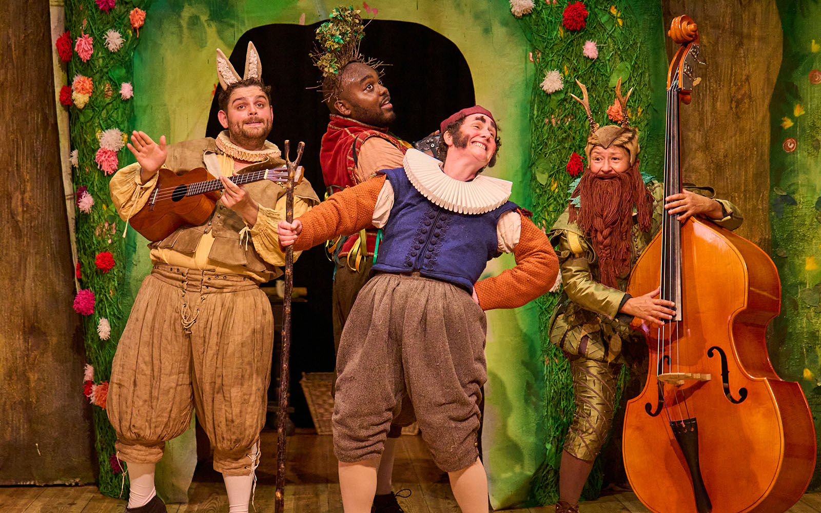 Full company of Midsummer Mechanicals. They all wear waistcoats and breeches. Sam Glen holds a ukulele and wears rabbit ears, while Jamal Franklin wears a headband with branches sticking out of the top. Kerry Frampton holds a walking stick and wears sideburns, while Melody Brown plays a double bass and wears a beard.